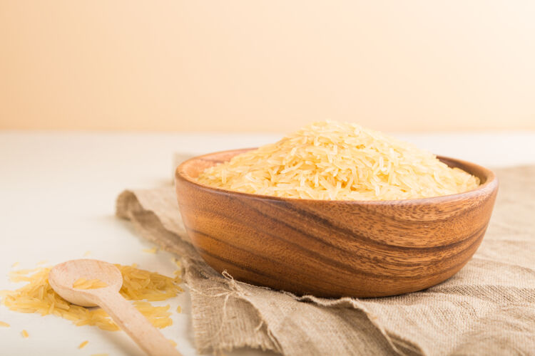 新鲜木制碗 生的金色米饭和白色木质表面和亚麻织物上的木勺中国木材美食