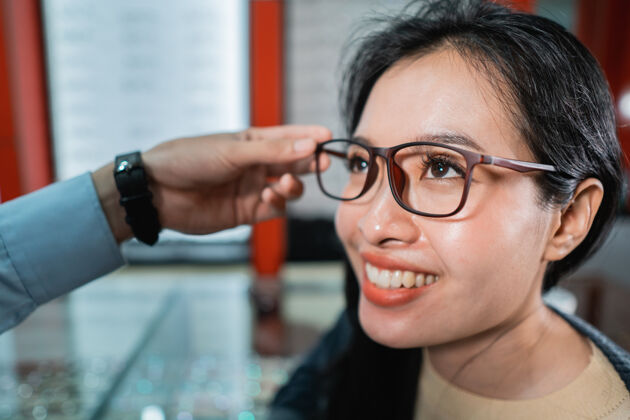 眼镜一名员工的手正在帮助戴上一副眼镜 这副眼镜是一位做过眼科检查的女士在眼科诊所挑选的视力验光师职业