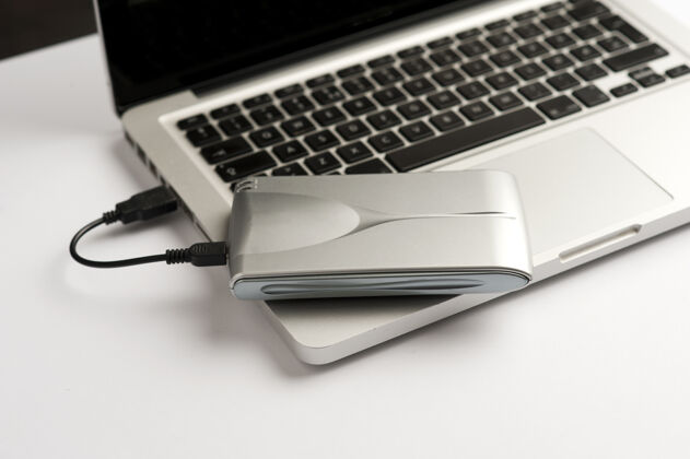 电脑铝制外置硬盘 带usb电缆 位于白色办公桌上的笔记本电脑顶部屏幕桌面外部