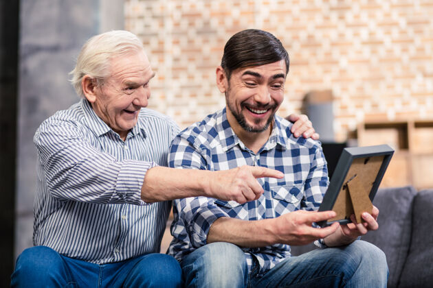 退休快乐的父子俩看着相框微笑着成年老人护理