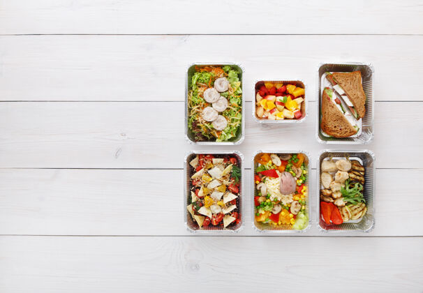 顶视图健康食品配送 日常膳食和零食营养 蔬菜 肉类和水果在铝箔盒俯视图 平放在白色木材与复制空间平铺晚餐蔬菜
