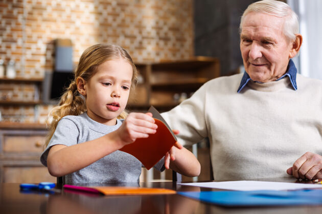 艺术可爱的小女孩一边叠着纸 一边和爷爷做节日贺卡童年桌子纸