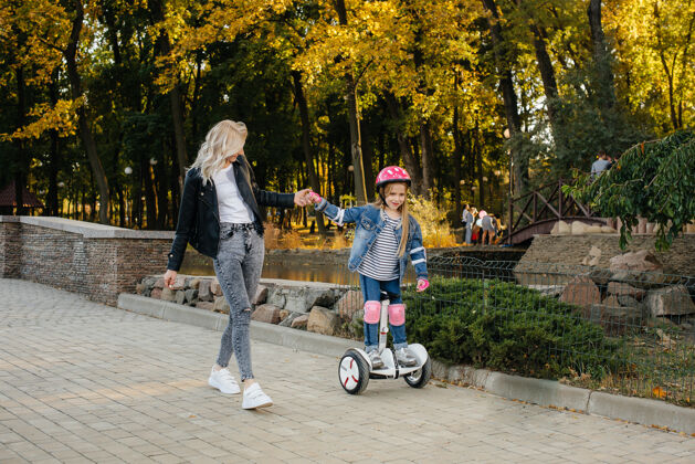 日落一位母亲在日落时分教她的小女儿在公园里骑赛格威家庭假期快乐头盔车辆享受