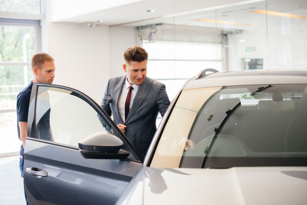 购买一个年轻的商人和一个推销员在汽车经销店看一辆新车买一辆车咨询租赁销售