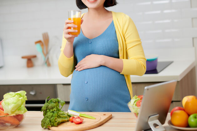 怀孕孕妇在厨房喝健康果汁身体亚洲沙拉