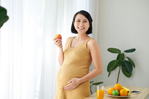 亚洲孕妇站在桌子旁边 手里拿着一盘新鲜水果怀孕苹果中国