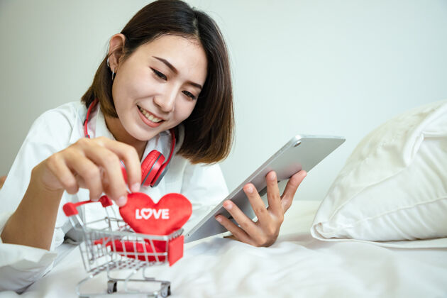 在线亚洲美女用平板电脑在情人节买礼物和购物车用爱心短信人白色平板电脑
