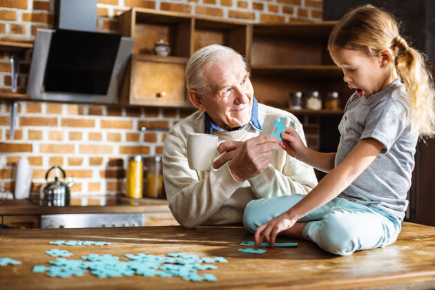 乐趣可爱的小女孩坐在桌子上 和爷爷一起拼图孙子学习爷爷