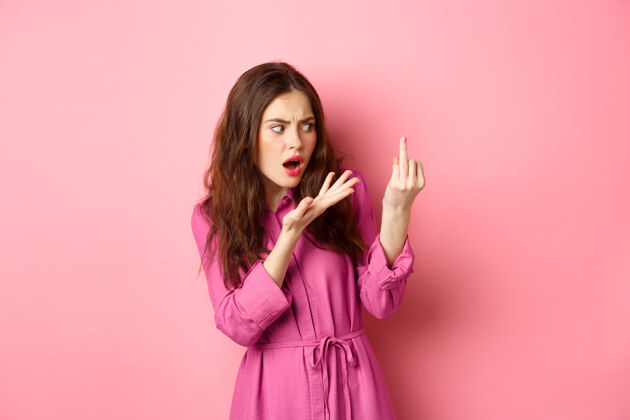 问题恼火的女朋友为求婚争吵 想结婚 没戴订婚戒指就伸出手指 困惑地站在粉红色的墙上关系概念时尚成人年轻