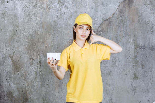 聪明人穿着黄色制服的女服务人员拿着一个塑料外卖碗 要求打电话预订货物工人