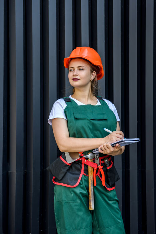 工人女工或builder.beautiful穿着工作服和头盔的女士在黑暗的背景下摆姿势腰带工作安全帽