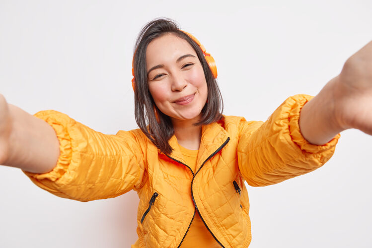 啦啦队可爱的亚洲年轻女子 一头黑发 身着橙色长裙 一边自拍 一边微笑 一边听音乐快乐夹克完美