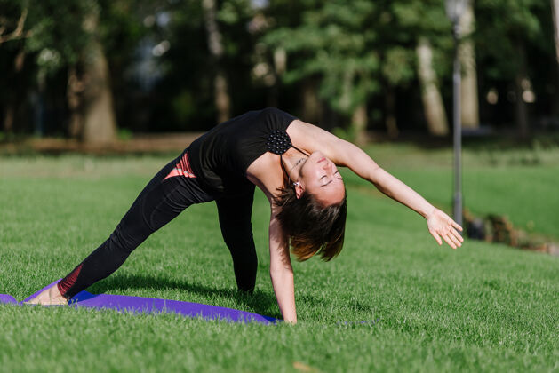 锻炼女孩在公园的草地上练瑜伽夏天一个女人在公园里做体式瑜伽体位早上