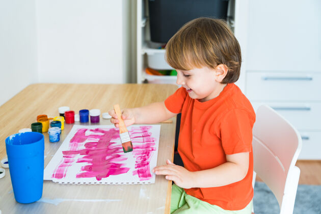 艺术品小男孩坐在书桌旁 用颜料画着五颜六色的图画童年艺术家彩色