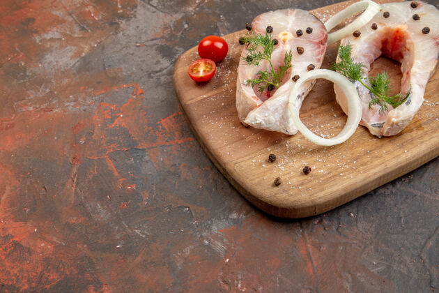 胡椒新鲜生鱼和胡椒洋葱绿色西红柿的特写镜头放在混合色表面的木质砧板上肉混合午餐