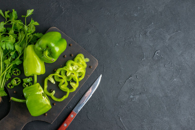板上图：绿色捆扎新鲜的整只青椒放在木质砧板上 刀放在右侧的黑色凹面上甜椒刀胡椒