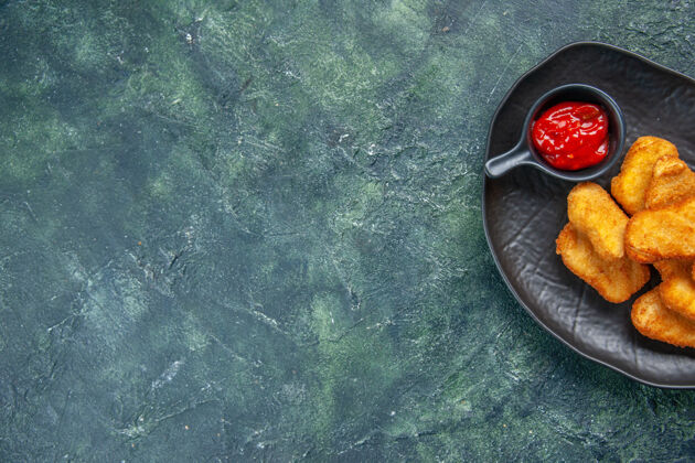 帽子半张美味的鸡块和番茄酱放在黑色的盘子里 放在黑暗的表面上 有足够的空间盘子子弹圆圈