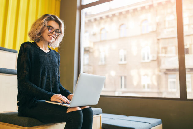 学生年轻漂亮的女人坐在教室的大窗户旁 用笔记本电脑工作 戴着眼镜互联网工作在线