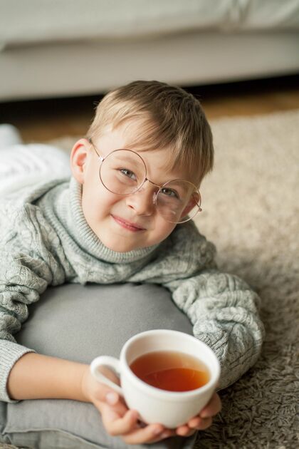 父母一个穿着针织毛衣的漂亮小男孩拿着一杯热咖啡在窗边看书茶舒适秋天秋天的心情概念聪明沟通