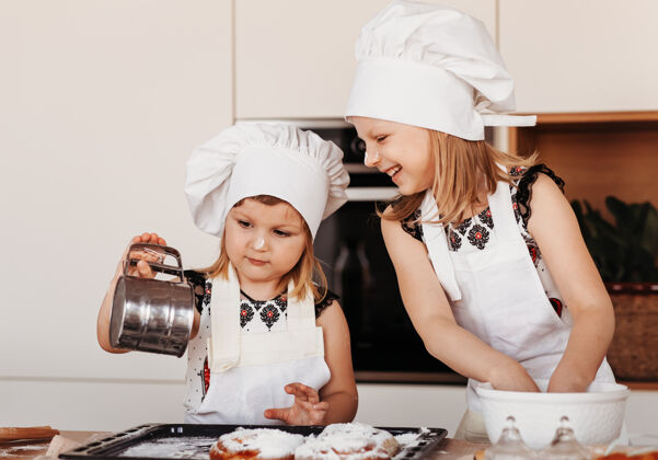 肖像两个戴着白色厨师帽的小女孩在教室里玩得很开心厨房.儿童做饭烘焙面包师女孩