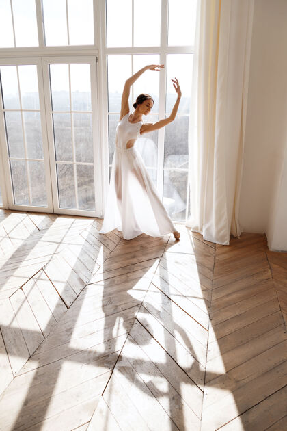 姿势穿着白裙子的舞者靠近窗户表演女士舞蹈