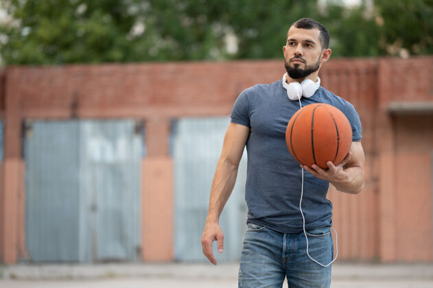 成功一个戴着耳机的男人站在街上 手里拿着一个篮球篮球网训练