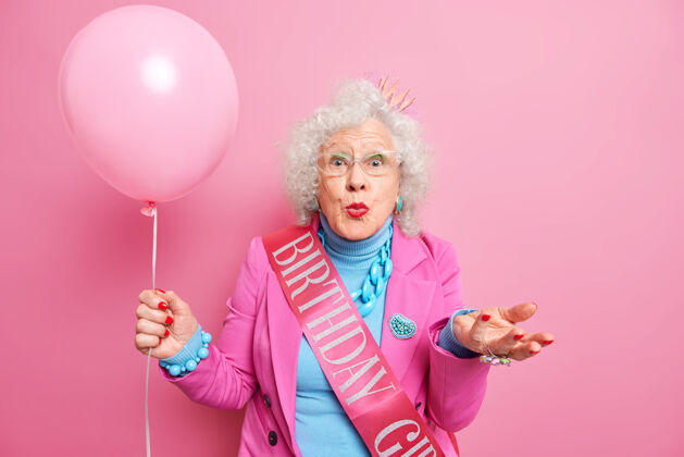 模型老人和节日的概念美丽的满脸皱纹的退休妇女保持嘴唇圆润举起手掌握着充气气球场合年龄服装