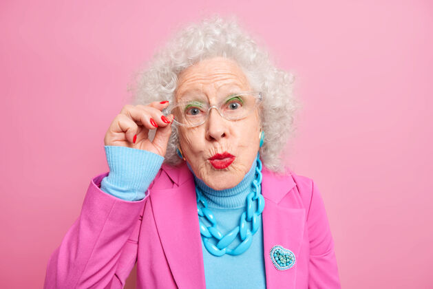 红一头灰色卷发的欧洲老太太的画像 手放在眼镜边 嘴唇圆润 穿着时髦的衣服女性时尚人