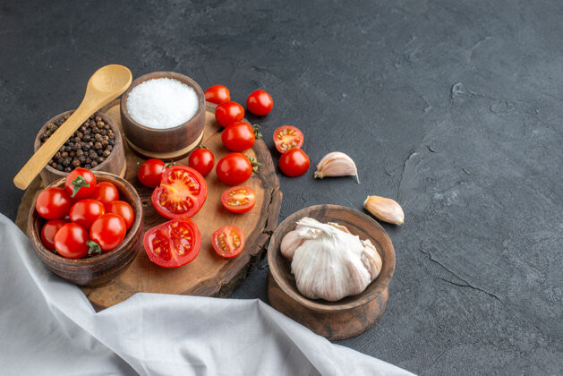 大蒜木板上新鲜西红柿和香料的特写镜头黑色表面上的白色毛巾大蒜素勺子容器健康