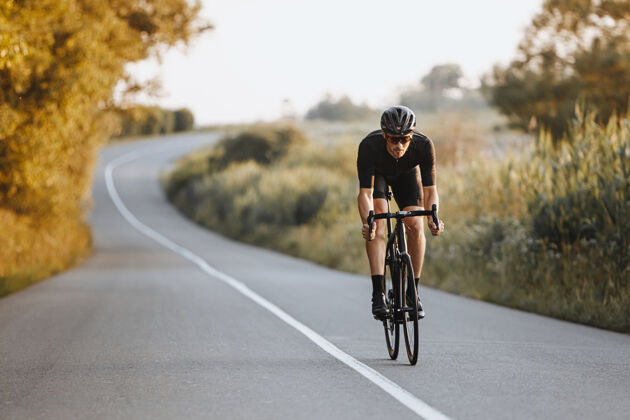 专业戴着黑色头盔 戴着防护眼镜 穿着运动服的专业男性自行车手 在背景模糊的路面上动态地骑着自行车快速眼镜自行车手