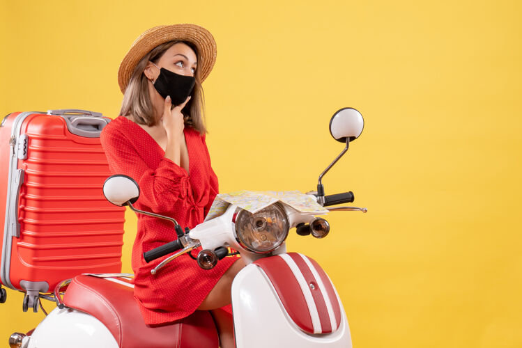 年轻女士前视图穿着红色衣服的年轻女士骑着轻便摩托车在想什么思考旅游手提箱