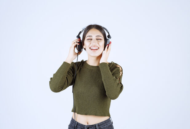 耳机在白色背景上聆听音乐的富有表现力的年轻女孩的画像魅力年轻情感