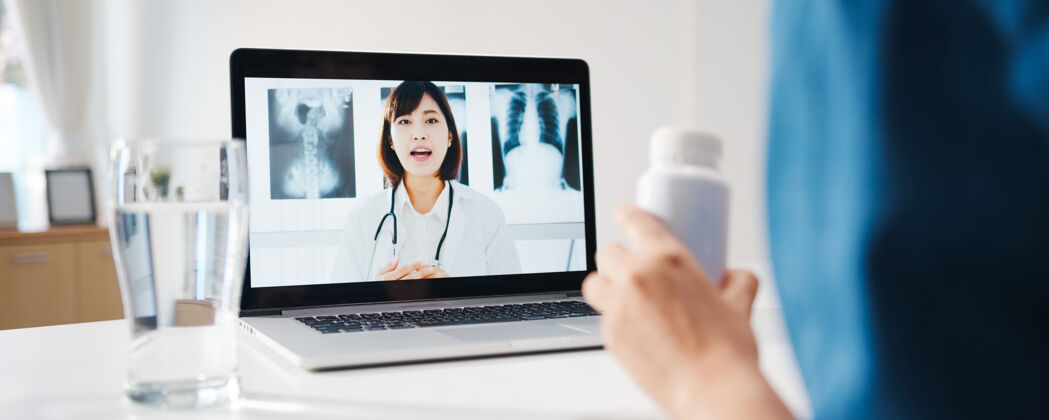 视频呼叫年轻的亚洲女士在家里的起居室里用笔记本电脑和资深医生在线电话会议谈论一种疾病隔离人帮助疾病