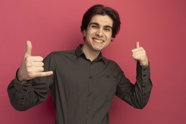 脸面带微笑的年轻帅哥 穿着黑色t恤 在粉红色的墙上显示着电话的手势穿着人表演