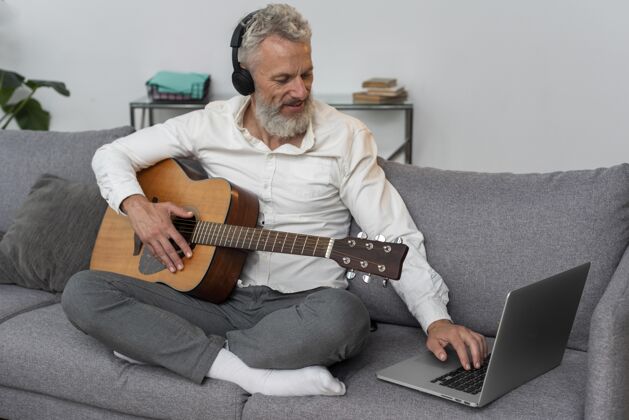 老年人老人在家的沙发上用笔记本电脑学习吉他课耳机内部原声吉他
