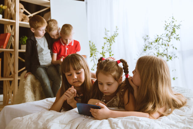肖像男孩和女孩在家里使用不同的小玩意孩子们带着智能手表 智能手机和耳机自拍 聊天 游戏 看视频孩子们和现代科技的互动孩子青少年上瘾