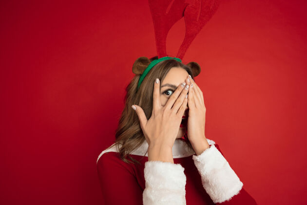 圣诞老人令人惊讶的隐藏的脸概念的圣诞节 新年 冬天的心情 假期…美丽的高加索女子长发像圣诞老人的驯鹿抓礼物盒快乐传统模特