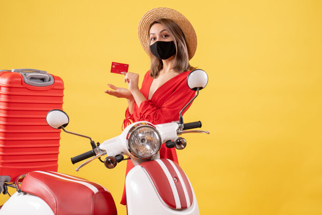 面罩正面图：戴巴拿马帽的年轻女子手持信用卡 靠近轻便摩托车信用旅游人