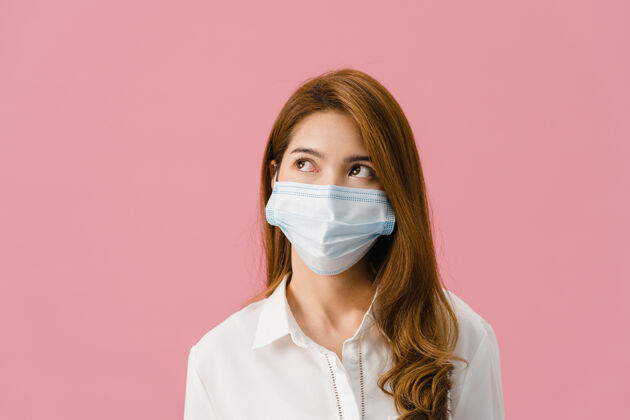 卫生年轻的亚洲女孩戴着医用面罩 穿着休闲服 看着粉色背景上的空白社交医学粉色