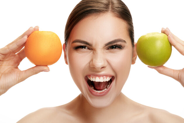 饮食美丽的白人微笑女人的肖像画 以绿色苹果和橙色水果为背景 与白色工作室隔离开来口腔成人微笑