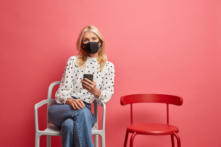 牛仔裤感染冠状病毒的妇女戴着防护面具独自一人在自我隔离时用手机查看新闻安全电话病毒
