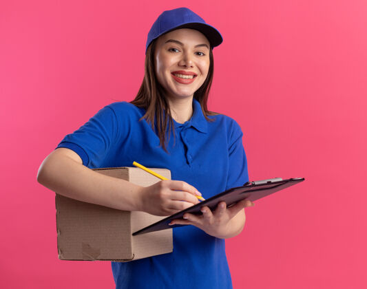 名片盒一个穿着制服 面带微笑的漂亮女送货员用铅笔在剪贴板上拿着卡片盒微笑粉色漂亮