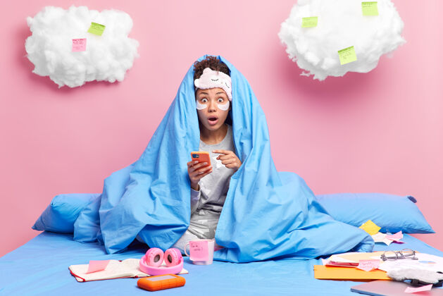 国内毛毯下的女人指着智能手机发现令人震惊的消息闲暇时间在家里戴着睡眠面罩睡衣做作业学习远包装书房指点