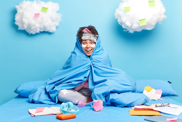 睡眠面罩隔离隔离期间 女孩在家远程学习 用blanet包装 使得mlist在便签上做的事情看起来很快乐 被隔离在蓝色的墙上房子高兴包装