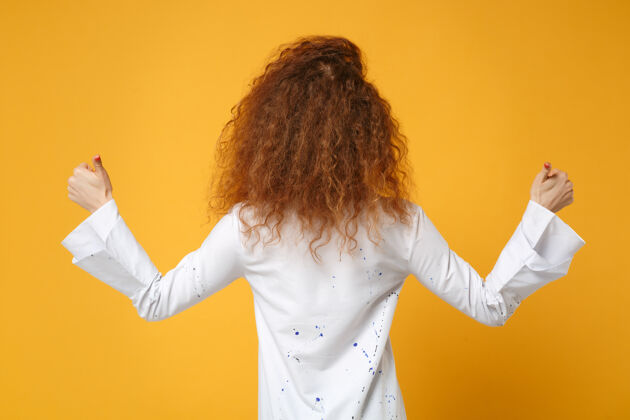 信号年轻的红发女女孩穿着休闲白衬衫 在黄橙色的墙上摆出孤立的姿势大拇指向上一手指