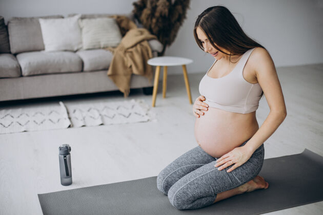 腹部孕妇在家里的垫子上练习瑜伽瑜伽产前怀孕