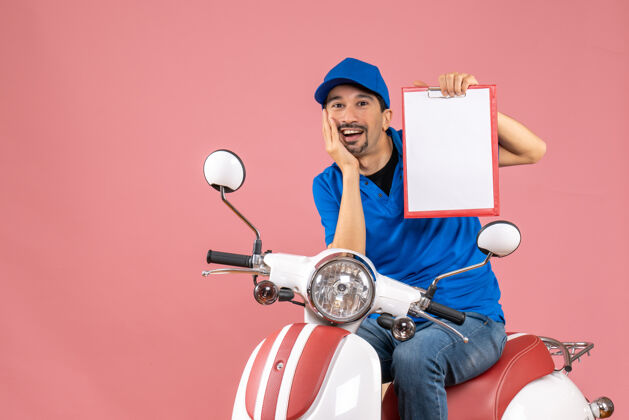 桃俯视图微笑的信使男子戴着帽子坐在滑板车上显示文件粉彩桃技术播放器帽子