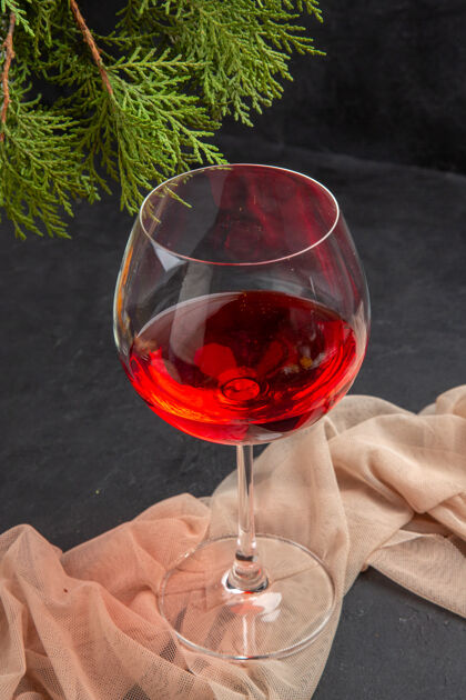 酒杯上图：美味的红酒放在毛巾上的玻璃高脚杯里 冷杉枝放在深色的背景上深色玻璃杯液体