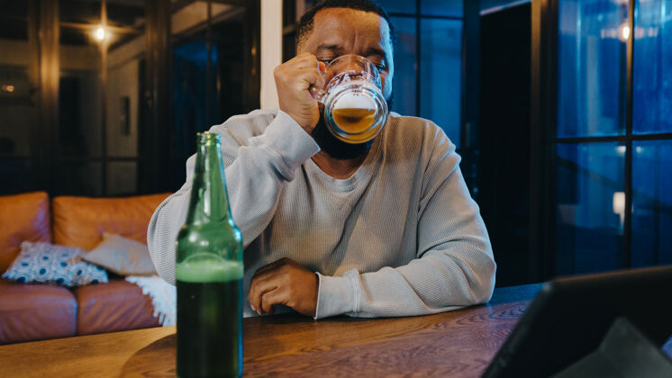酒瓶中年非洲裔美国男性在家中客厅通过视频通话 喝啤酒 享受快乐之夜派对活动在线庆祝活动放松黑人互联网