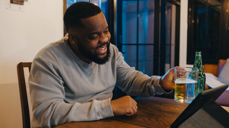 酒精中年非洲裔美国男性在家中客厅通过视频通话 喝啤酒 享受快乐之夜派对活动在线庆祝活动庆祝人虚拟